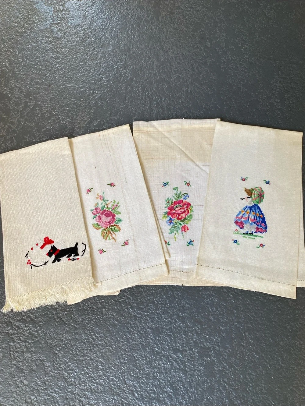 The image shows a set of four vintage hand-embroidered and cross-stitched